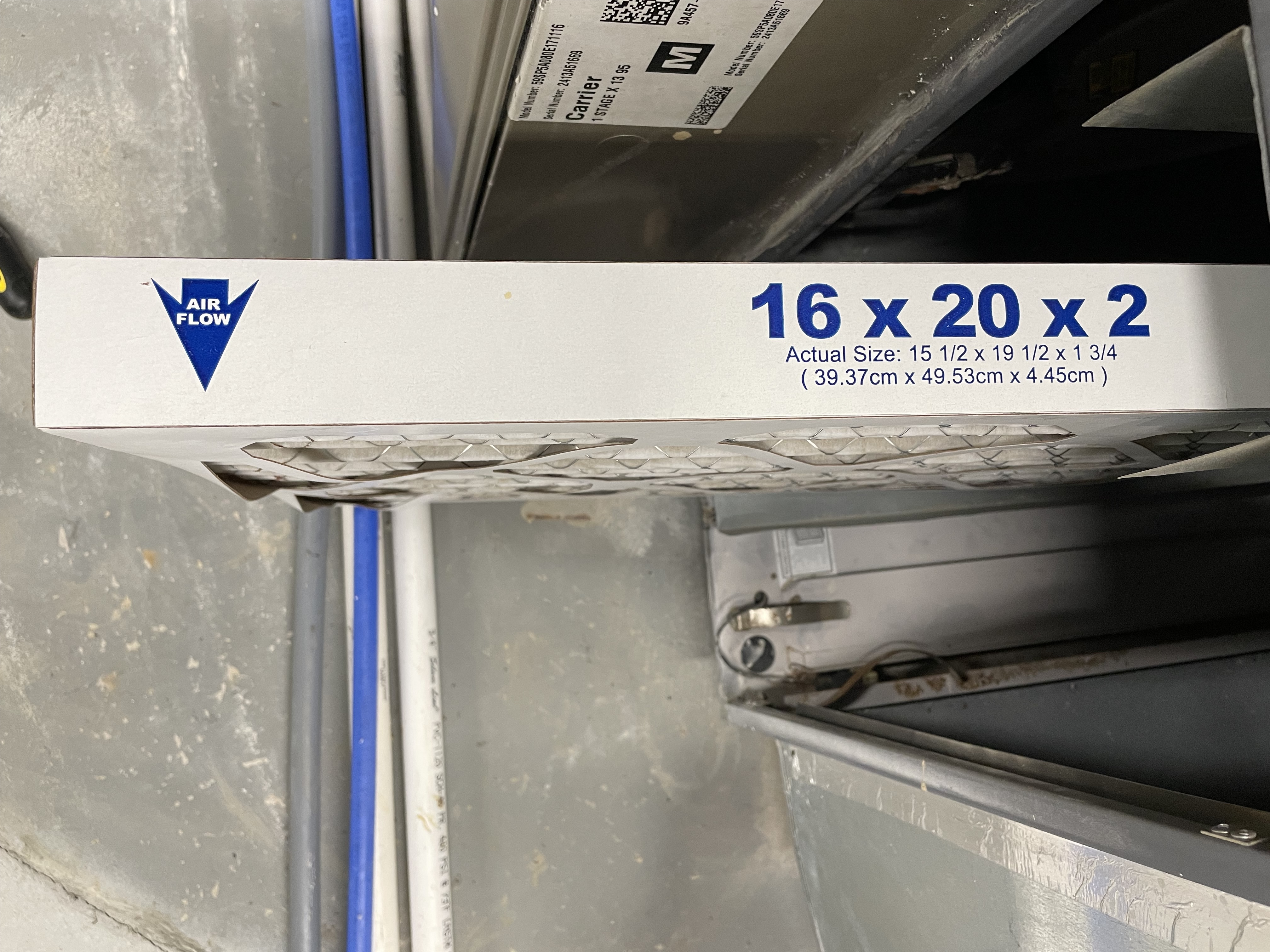 Photo of an air filter being slid into place in an HVAC unit. On one end an arrow says "air flow" and shows which direction to put the filter in. Along the edge, the size is listed.