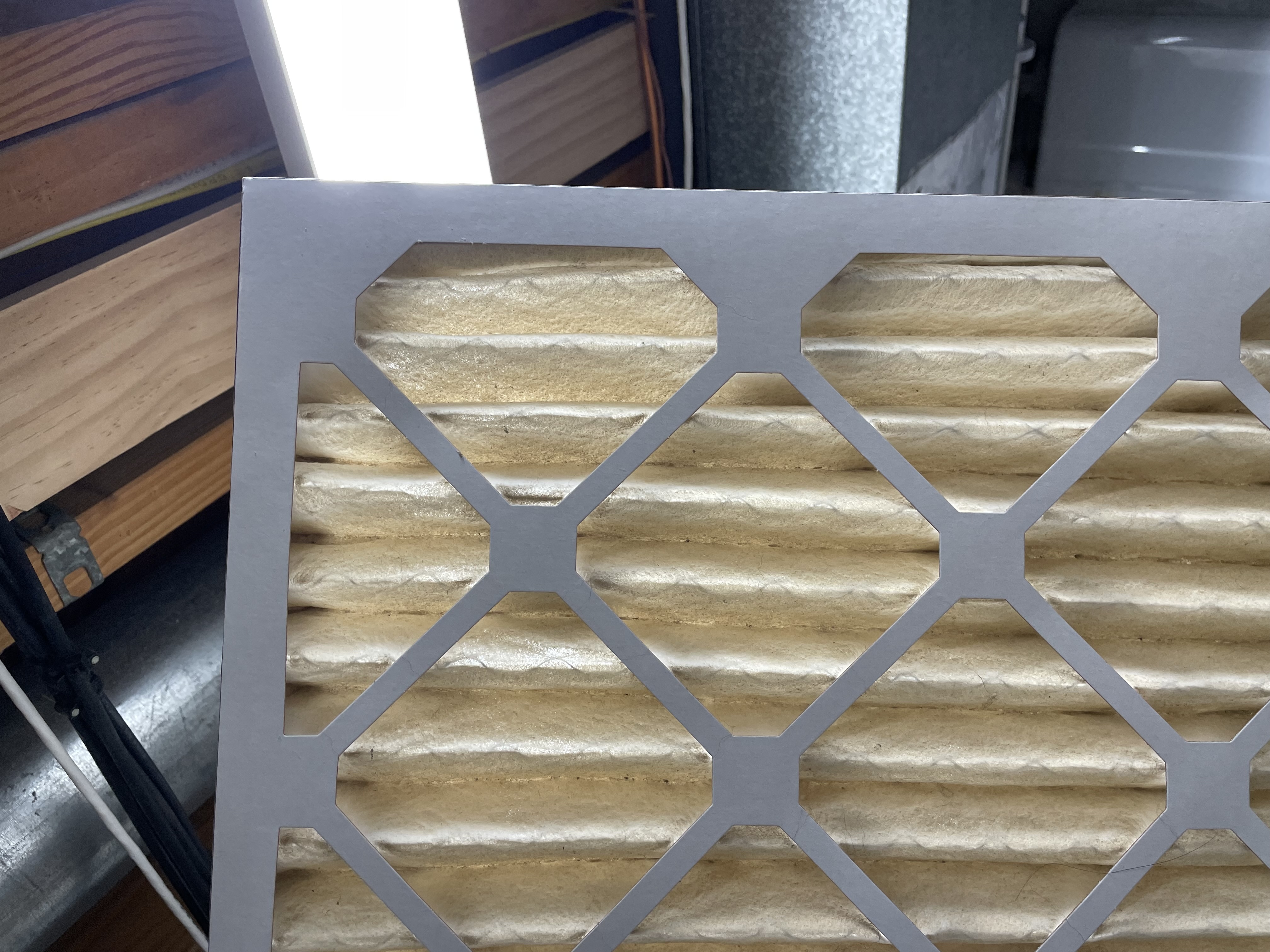 An HVAC filter is held up to the light to see if it's time to change. Very little light passes through, which indicates it's clogged with dirt and should be replaced.